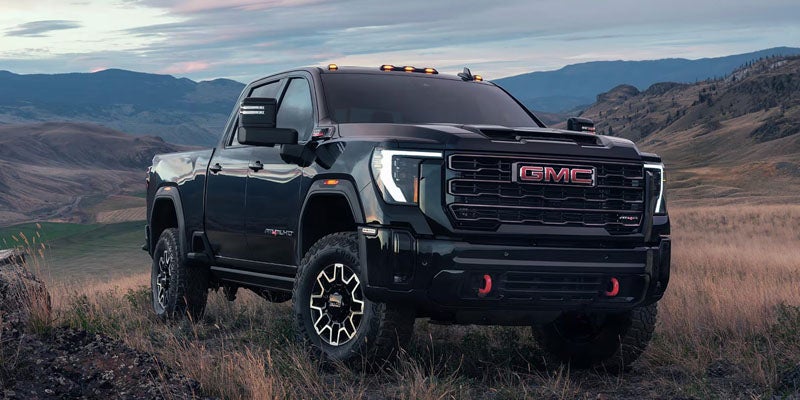 A black 2026 GMC Sierra 2500 truck is sitting in the middle of a wide open field with mountains quite far away surrounding it in the background.