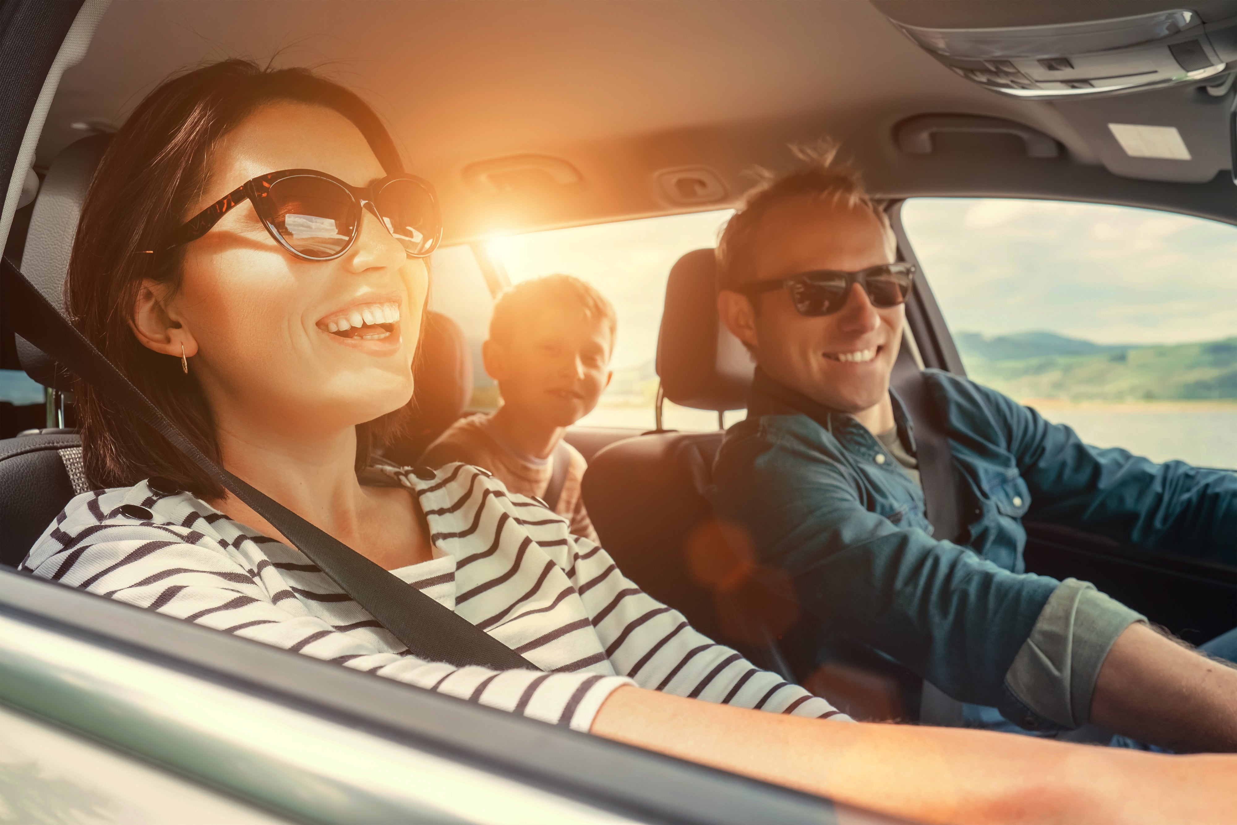 A couple are smiling and laughing along with their son as they are on a sunshiny family road trip in a GMC vehicle.